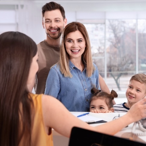 Family smiling at dental office reception desk