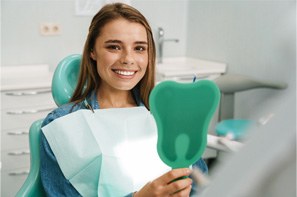 Young woman smiling while holding green handheld mirror