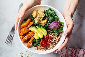 Hands holding white bowl full of healthy foods over marble counter