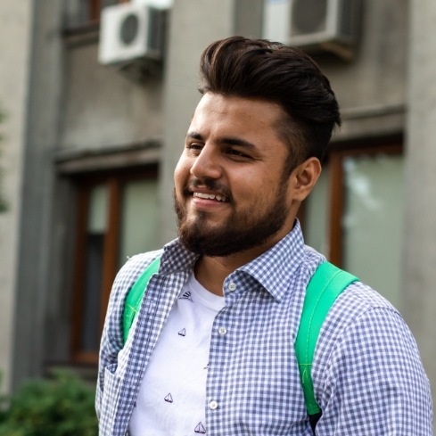 Young man wearing green backpack and blue plaid shirt outdoors