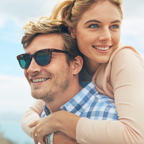 Young woman hugging young man in sunglasses from behind