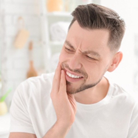 Man in white shirt holding teeth due to tooth pain