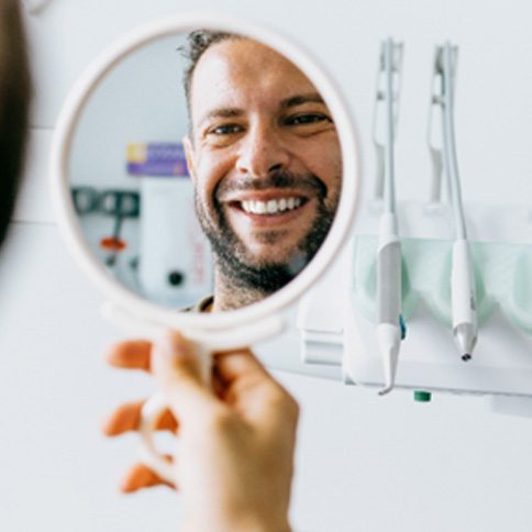 Man smiling in reflection of small dental mirror